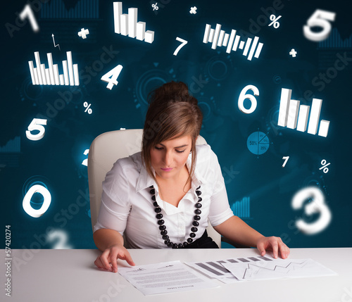 Photo: Young businesswoman sitting at desk with diagrams and statistics Young businesswoman sitting at desk with diagrams and statistics