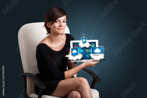 Photo: young woman holding tablet with modern devices in clouds young woman holding tablet with modern devices in clouds