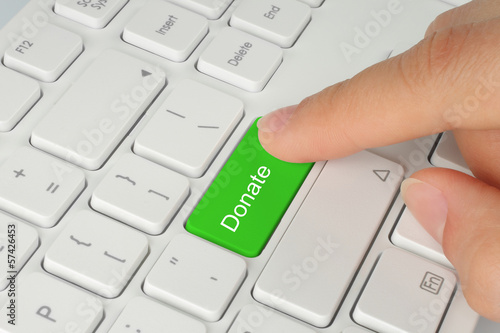 Photo: Hand pushing green donate button on white keyboard. Hand pushing green donate button on white keyboard.