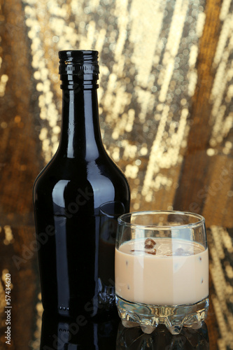 Photo: Baileys liqueur in bottle and glass on golden background Baileys liqueur in bottle and glass on golden background