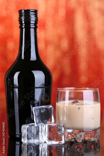 Photo: Baileys liqueur in bottle and glass on red background Baileys liqueur in bottle and glass on red background