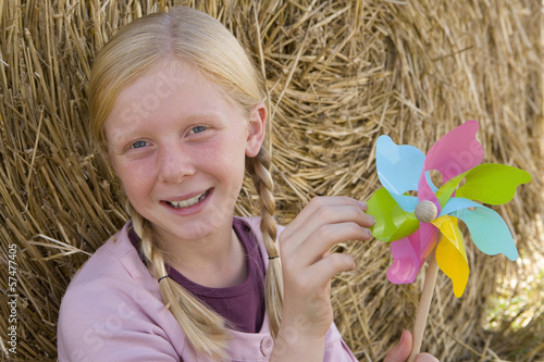 Photo: Girl (11-13) by bale of hay with pinwheel, smiling, portrait Girl (11-13) by bale of hay with pinwheel, smiling, portrait