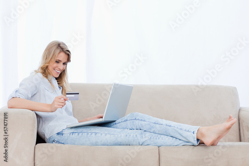 Photo: A woman lying on a couch with a laptop in front of her is holdin A woman lying on a couch with a laptop in front of her is holdin