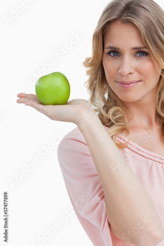Photo: Young woman holding a green apple while looking at the camera Young woman holding a green apple while looking at the camera