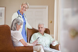 Photo: Smiling home caregiver talking to senior couple with digital tablets in armchairs Smiling home caregiver talking to senior couple with digital tablets in armchairs