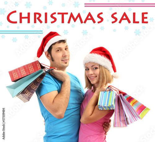 Photo: Young couple in Santa hats shopping and holding many shopping Young couple in Santa hats shopping and holding many shopping