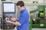 Photo: Technician measuring gear wheel with vernier caliper in front of lathe cutting machine in hi-tech manufacturing plant Technician measuring gear wheel with vernier caliper in front of lathe cutting machine in hi-tech manufacturing plant