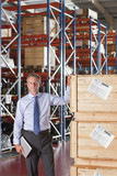 Photo: Portrait of confident businessman holding digital tablet and leaning on crates in warehouse Portrait of confident businessman holding digital tablet and leaning on crates in warehouse