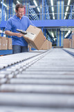 Photo : Worker with bar code reader scanning box on conveyor belt in distribution warehouse Worker with bar code reader scanning box on conveyor belt in distribution warehouse