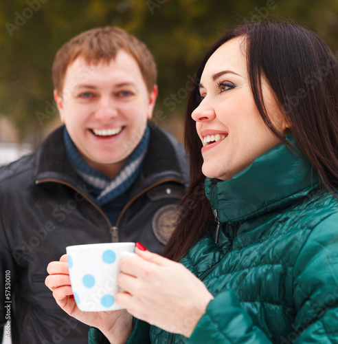 Photo: Happy couple having fun in the winter park drinking hot tea Happy couple having fun in the winter park drinking hot tea