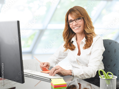 Photo: Smiling businesswoman at office desk with a computer Smiling businesswoman at office desk with a computer