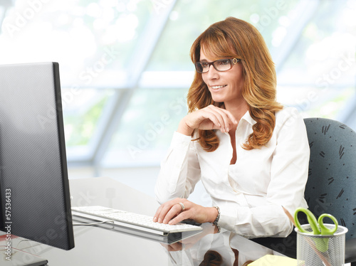 Photo: Smiling businesswoman at office desk with a computer Smiling businesswoman at office desk with a computer