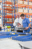 Photo: Supervisor and worker examining machine parts in bin on production line in distribution warehouse Supervisor and worker examining machine parts in bin on production line in distribution warehouse