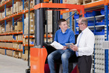 Foto: Supervisor and worker with paperwork and digital tablet next to forklift in distribution warehouse Supervisor and worker with paperwork and digital tablet next to forklift in distribution warehouse