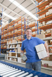 Photo: Portrait of smiling worker holding scanner and boxes at production line in distribution warehouse Portrait of smiling worker holding scanner and boxes at production line in distribution warehouse