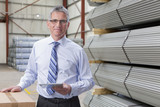 Photo: Portrait of smiling supervisor with digital tablet next to steel bars in warehouse Portrait of smiling supervisor with digital tablet next to steel bars in warehouse