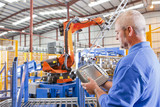 Photo: Worker controlling robotic machinery lifting steel fencing on production line in manufacturing plant Worker controlling robotic machinery lifting steel fencing on production line in manufacturing plant