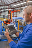 Photo: Close up of worker controlling robotic machinery lifting steel fencing on production line in manufacturing plant Close up of worker controlling robotic machinery lifting steel fencing on production line in manufacturing plant