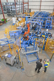 Photo: Businessman and worker controlling robotic machinery lifting steel fencing on production line in manufacturing plant Businessman and worker controlling robotic machinery lifting steel fencing on production line in manufacturing plant