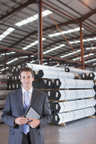 Photo: Portrait of smiling businessman with digital tablet in front of steel tubing in warehouse Portrait of smiling businessman with digital tablet in front of steel tubing in warehouse