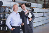 Photo: Bank manager and businessman with digital tablet talking in front of steel tubing in warehouse Bank manager and businessman with digital tablet talking in front of steel tubing in warehouse