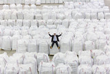 Photo: Portrait of enthusiastic businessman sitting on top of large bags of recycled plastic pellets in warehouse Portrait of enthusiastic businessman sitting on top of large bags of recycled plastic pellets in warehouse