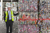 Photo: Portrait of confident businessman leaning on bales of recycled plastic in recycling plant Portrait of confident businessman leaning on bales of recycled plastic in recycling plant