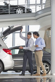 Photo: Salesman and customer with brochure looking into hatchback of car in car dealership showroom Salesman and customer with brochure looking into hatchback of car in car dealership showroom