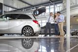 Photo: Salesman and couple with brochure looking into hatchback of car in car dealership showroom Salesman and couple with brochure looking into hatchback of car in car dealership showroom