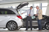 Foto: Salesman and customer with brochure looking into hatchback of car in car dealership showroom Salesman and customer with brochure looking into hatchback of car in car dealership showroom