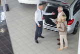 Photo: Salesman showing couple with brochure hatchback of car in car dealership showroom Salesman showing couple with brochure hatchback of car in car dealership showroom