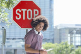 Photo: Portrait of smiling young man with headphones using digital tablet against stop sign in city Portrait of smiling young man with headphones using digital tablet against stop sign in city