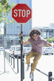 Photo: Portrait of enthusiastic young man listening to music on headphones against stop sign in city Portrait of enthusiastic young man listening to music on headphones against stop sign in city