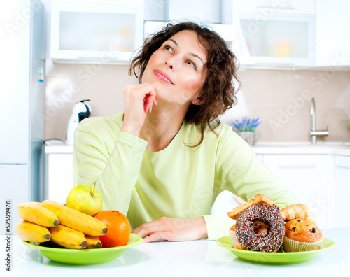 Photo: Dieting concept. Young Woman choosing between Fruits and Sweets Dieting concept. Young Woman choosing between Fruits and Sweets