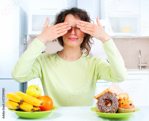 Photo: Dieting concept. Young Woman choosing between Fruits and Sweets Dieting concept. Young Woman choosing between Fruits and Sweets