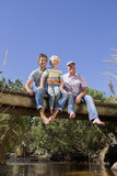 Photo: Portrait of smiling multi-generation family sitting barefoot on footbridge over stream Portrait of smiling multi-generation family sitting barefoot on footbridge over stream