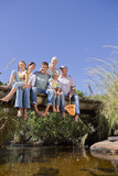 Photo: Portrait of smiling multi-generation family sitting barefoot on footbridge over stream Portrait of smiling multi-generation family sitting barefoot on footbridge over stream
