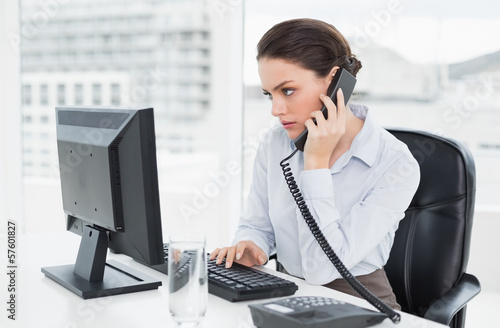 Photo: Elegant businesswoman using landline phone and computer in offic Elegant businesswoman using landline phone and computer in offic