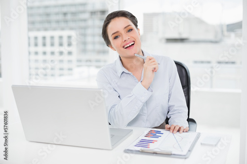 Photo: Happy businesswoman with graphs and laptop in office Happy businesswoman with graphs and laptop in office