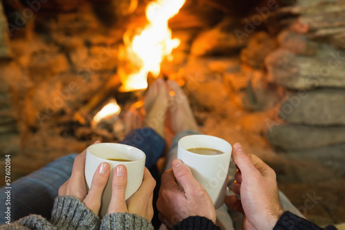 Photo: Hands holding coffee cups in front of lit fireplace Hands holding coffee cups in front of lit fireplace