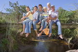 Photo: Portrait of smiling multi-generation family sitting barefoot on footbridge over stream Portrait of smiling multi-generation family sitting barefoot on footbridge over stream