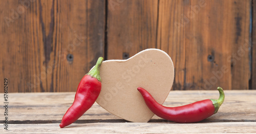 Photo: red chilly peppers with cardboard heart on wood background red chilly peppers with cardboard heart on wood background