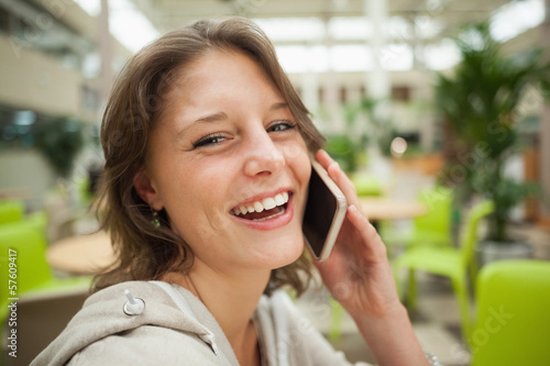 Photo: Cheerful woman using mobile phone in the cafeteria Cheerful woman using mobile phone in the cafeteria