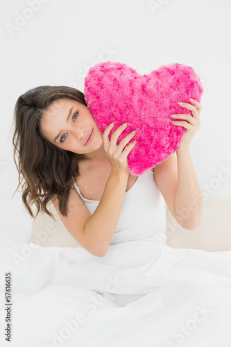 Photo: Cute woman holding heart shaped pillow in bed Cute woman holding heart shaped pillow in bed