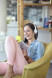 Photo: Smiling woman text messaging with cell phone and listening to music on headphones with digital tablet Smiling woman text messaging with cell phone and listening to music on headphones with digital tablet