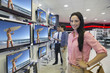 Photo: Portrait of smiling woman looking at flat screen televisions in electronics store Portrait of smiling woman looking at flat screen televisions in electronics store