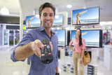 Photo: Portrait of smiling man holding remote control in front of televisions in electronics store Portrait of smiling man holding remote control in front of televisions in electronics store
