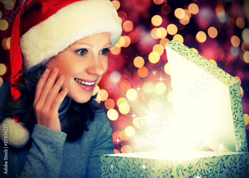 Photo: happy woman in a Christmas cap opens the magic box happy woman in a Christmas cap opens the magic box