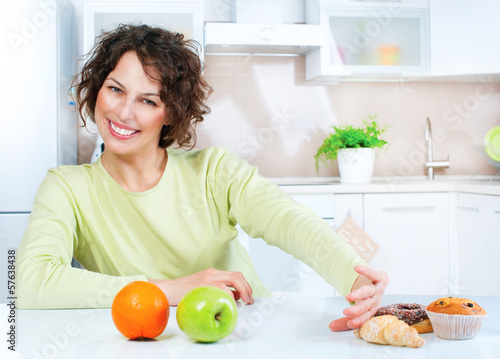Photo: Dieting concept. Young Woman choosing between Fruits and Sweets Dieting concept. Young Woman choosing between Fruits and Sweets
