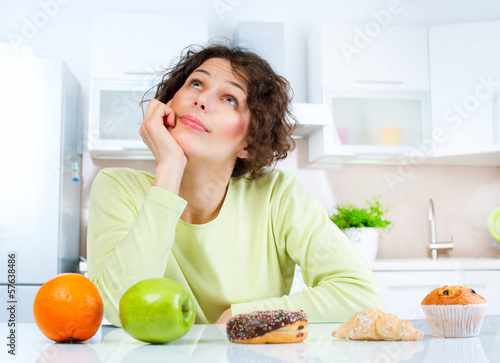 Photo: Dieting concept. Young Woman choosing between Fruits and Sweets Dieting concept. Young Woman choosing between Fruits and Sweets